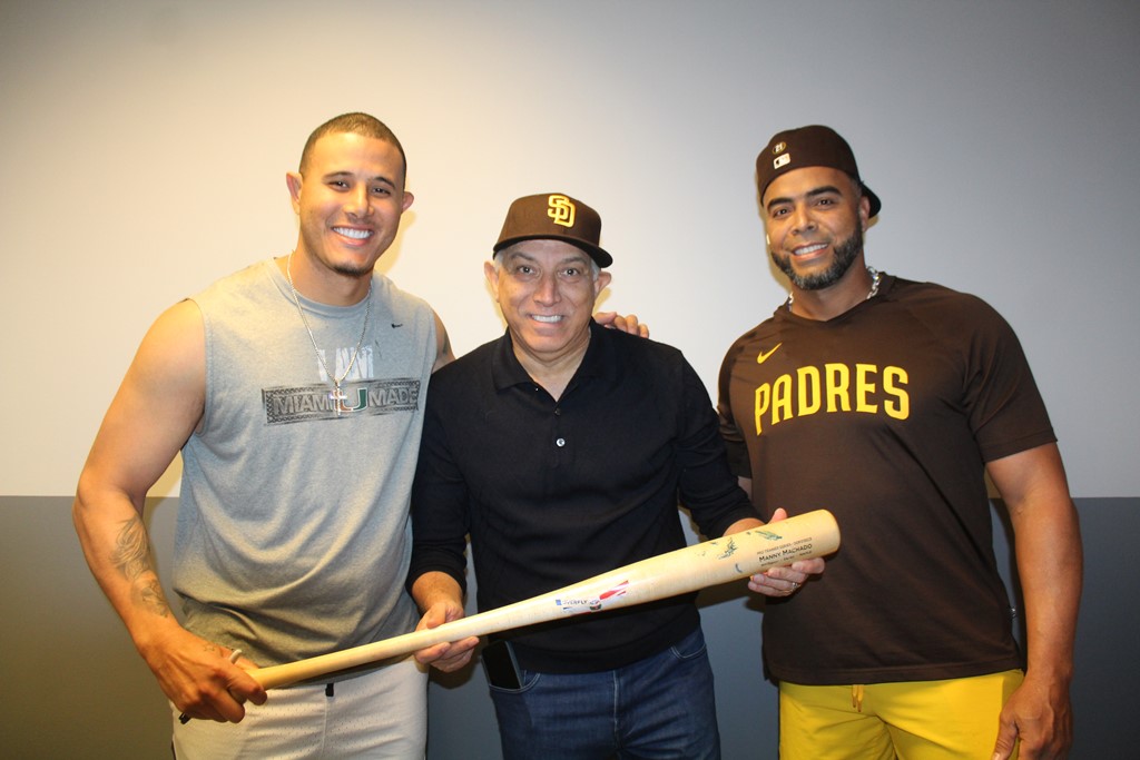 Manny Machado, (izq.), entrega un bate autografiado al doctor Ramón Tallaj, mientras Nelson Cruz, (der.), participa.